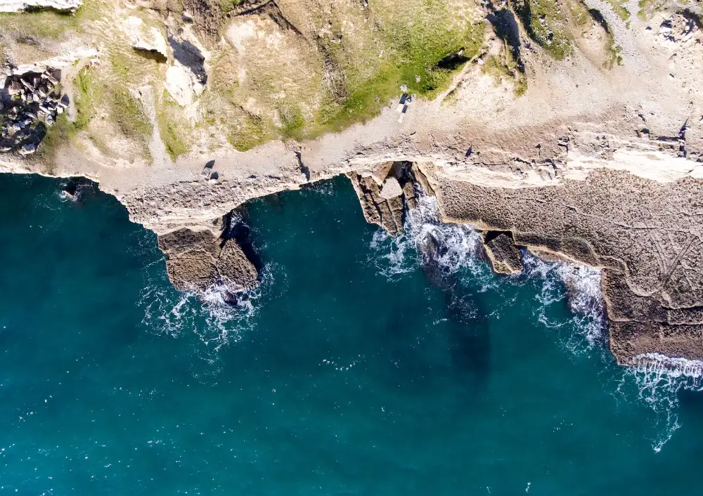 Photograph taken directly from above of a rocky coastline and a deep blue sea.